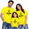 Family of three wearing bright yellow matching family T-shirts with black crown and heart designs, featuring The Spoiler on both adult shirts and The Spoiled One on the child's T-shirt.